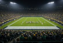 Falcons Rout Packers 35-14 as Michael Penix Jr. Returns From Torn ACL Night view across a packed stadium as players in white and dark green uniforms line up on a floodlit football field.