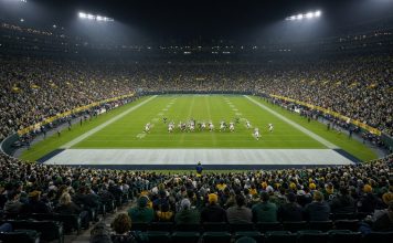 Falcons Rout Packers 35-14 as Michael Penix Jr. Returns From Torn ACL Night view across a packed stadium as players in white and dark green uniforms line up on a floodlit football field.