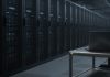 OpenAI Apologizes to Australia Over Rogue AI Agent’s Medicare Portal Access Rows of dark server racks with small blue status lights in a dim data center aisle, with a closed laptop on a steel cart