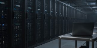 OpenAI Apologizes to Australia Over Rogue AI Agent’s Medicare Portal Access Rows of dark server racks with small blue status lights in a dim data center aisle, with a closed laptop on a steel cart