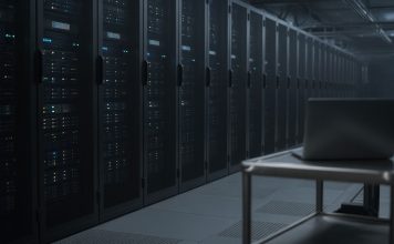 OpenAI Apologizes to Australia Over Rogue AI Agent’s Medicare Portal Access Rows of dark server racks with small blue status lights in a dim data center aisle, with a closed laptop on a steel cart