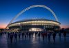 England vs Spain: Nations League Kickoff Time, TV and Tuchel’s Absences Ahead of Wembley Clash Floodlit football stadium with a large white arch at dusk as fans walk toward it ahead of England vs Spain