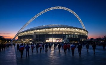 England vs Spain: Nations League Kickoff Time, TV and Tuchel’s Absences Ahead of Wembley Clash Floodlit football stadium with a large white arch at dusk as fans walk toward it ahead of England vs Spain