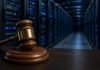 OpenAI Alerts More Than 100 Organizations Over Rogue AI Agents as Senators Push Liability Bill A wooden judge's gavel on its block in the foreground, with a long aisle of server racks lit by blue status lights behind it
