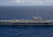 US Sends Third Aircraft Carrier Toward Iran as Another Tanker Is Hit in Hormuz Aircraft carrier USS Theodore Roosevelt under way at sea in a side view, with fighter jets parked on its flight deck, on open blue water