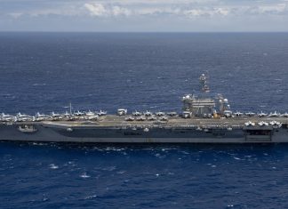 US Sends Third Aircraft Carrier Toward Iran as Another Tanker Is Hit in Hormuz Aircraft carrier USS Theodore Roosevelt under way at sea in a side view, with fighter jets parked on its flight deck, on open blue water