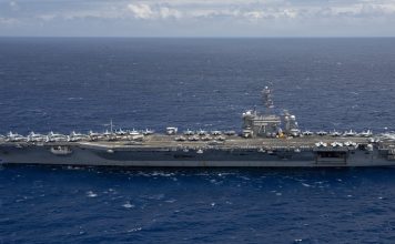 US Sends Third Aircraft Carrier Toward Iran as Another Tanker Is Hit in Hormuz Aircraft carrier USS Theodore Roosevelt under way at sea in a side view, with fighter jets parked on its flight deck, on open blue water