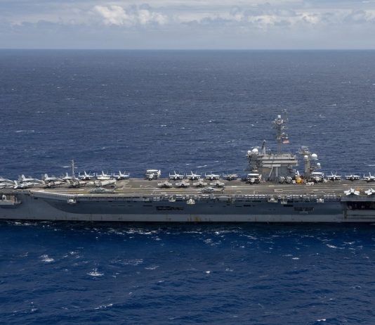 US Sends Third Aircraft Carrier Toward Iran as Another Tanker Is Hit in Hormuz Aircraft carrier USS Theodore Roosevelt under way at sea in a side view, with fighter jets parked on its flight deck, on open blue water