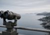 North Korea Fires Ballistic Missile After Seoul Demands Apology Over DMZ Mine Blast Mounted observation binoculars on a metal railing overlooking a calm grey sea and a rocky coastline under an overcast morning sky