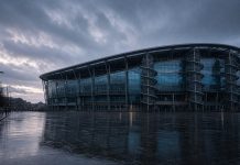 Manchester City Lodge Appeal Against Premier League Guilty Verdict: What Happens Next A modern football stadium with a curved glass facade and spiral access towers at dusk in the rain, with an empty wet plaza in front
