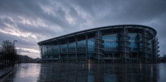 Manchester City Lodge Appeal Against Premier League Guilty Verdict: What Happens Next A modern football stadium with a curved glass facade and spiral access towers at dusk in the rain, with an empty wet plaza in front